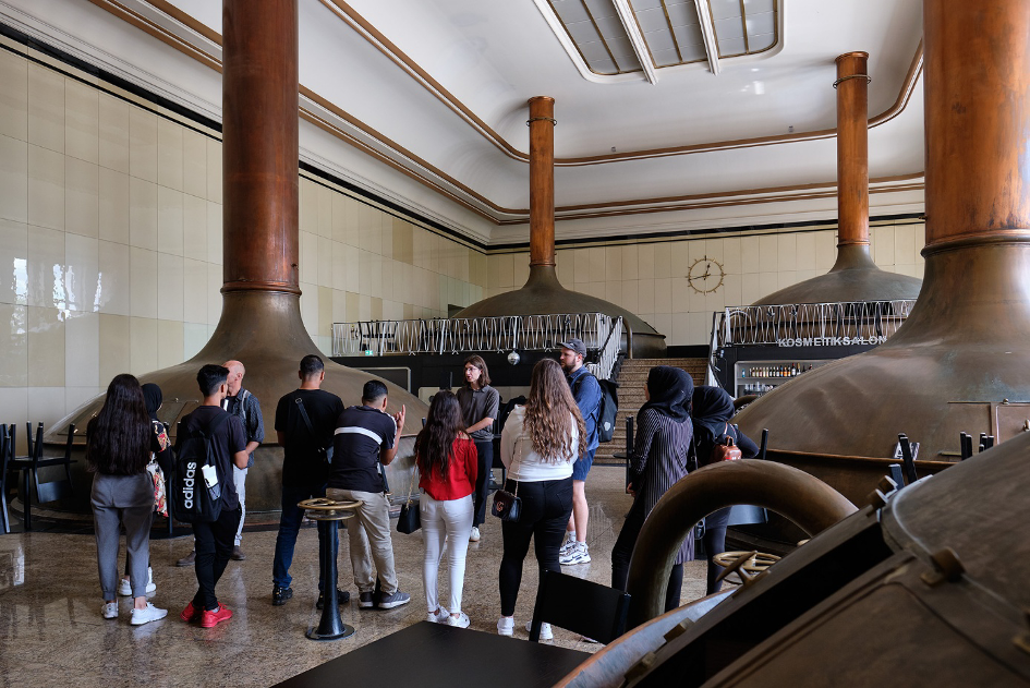 Eine Gruppe von Jugendlichen steht im Sudhaus der ehemaligen Kindl-Brauerei und hört dem Guide zu